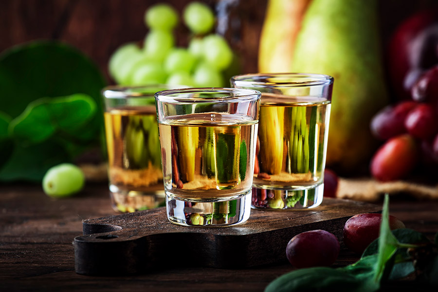 Regionale Liköre Drei kleine Gläser mit goldfarbenem Schnaps auf Holztisch, Trauben im Hintergrund.